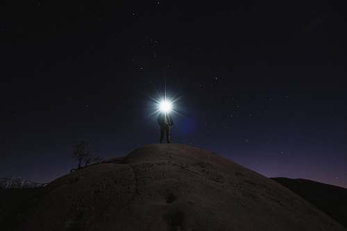 night sky man standing on mountain white holding flashlight stars